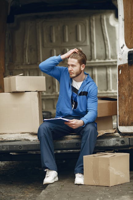 Two movers from Man with Van Silvertown are engaged in a home relocation process outside a modern building, with the loading area on a paved surface. One mover, a woman wearing a black jacket, white s